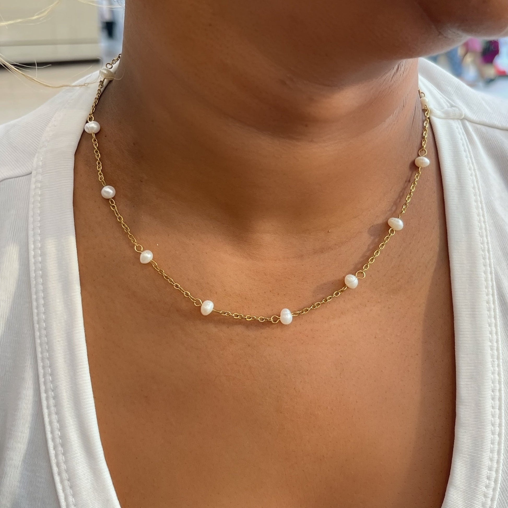 Close-up of a person wearing a gold necklace with pearls and gold earrings.
