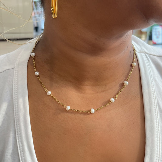 Close-up of a person wearing a gold necklace with pearl-like beads.