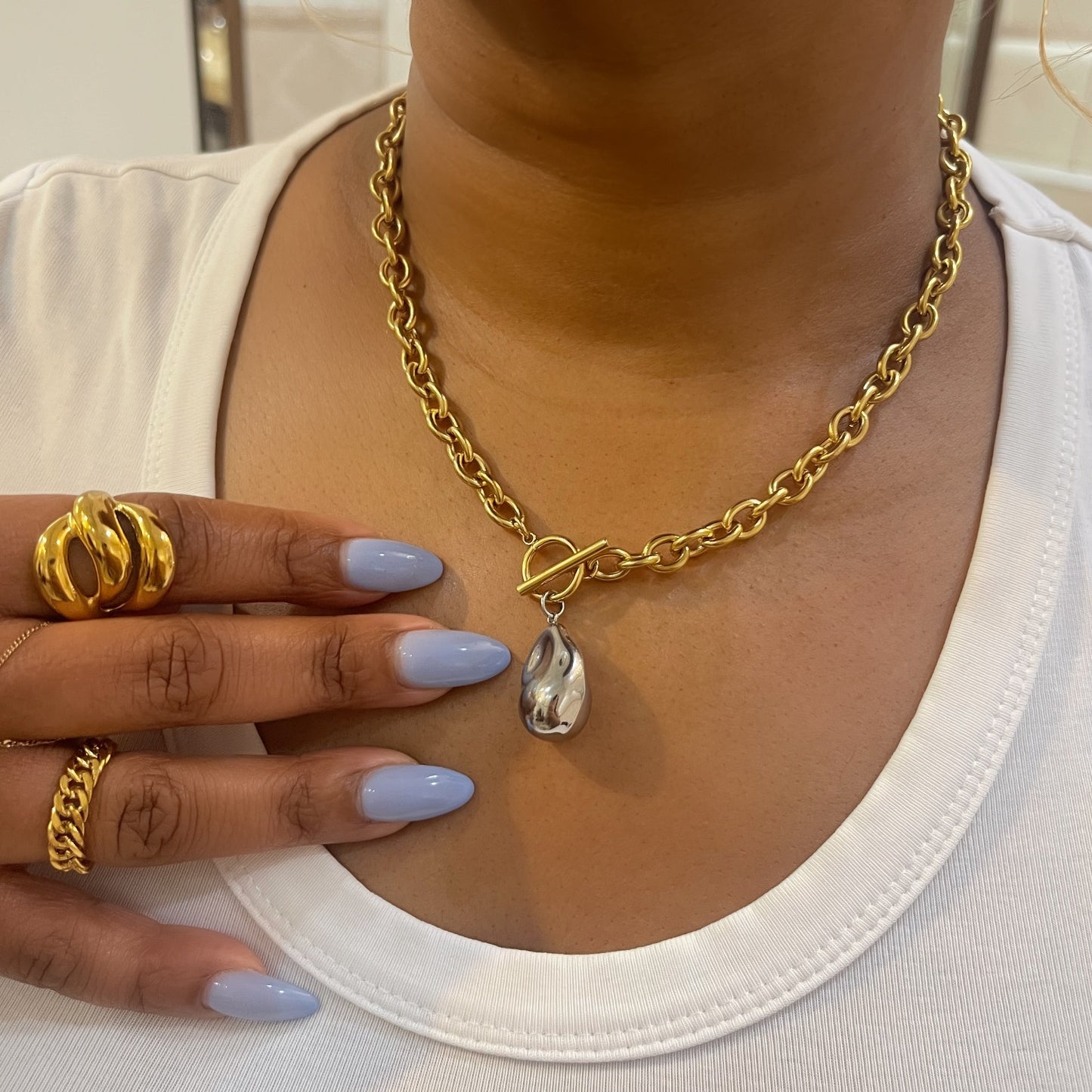 Person wearing a gold chain necklace with a pendant, holding a gold ring with a white background.