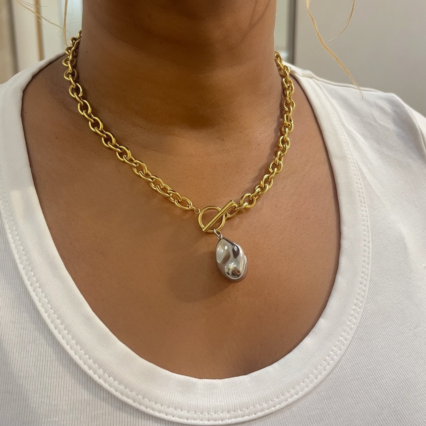 Gold chain necklace with a pendant worn by a person in a white shirt.
