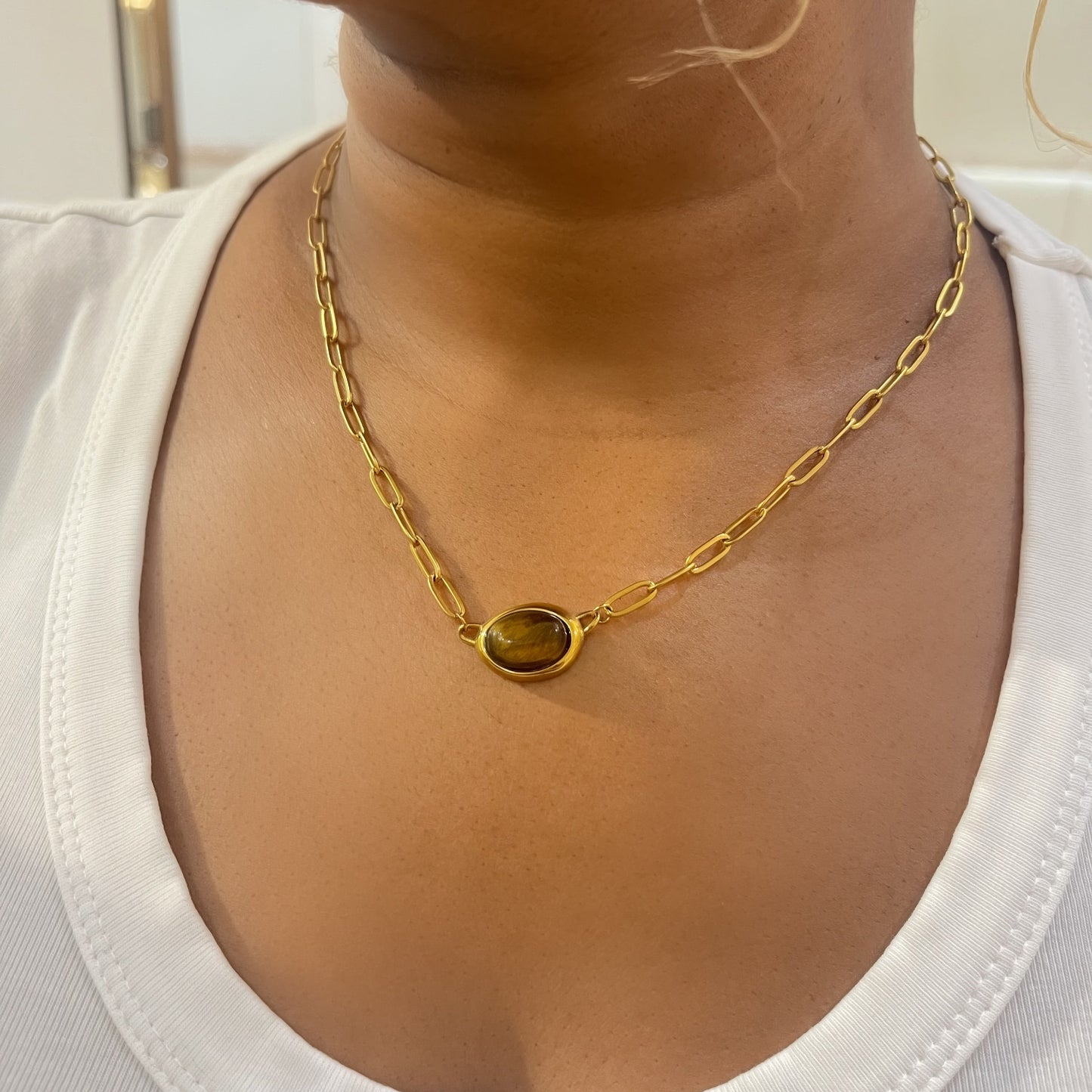 Gold chain necklace with a pendant on a person wearing a white top.