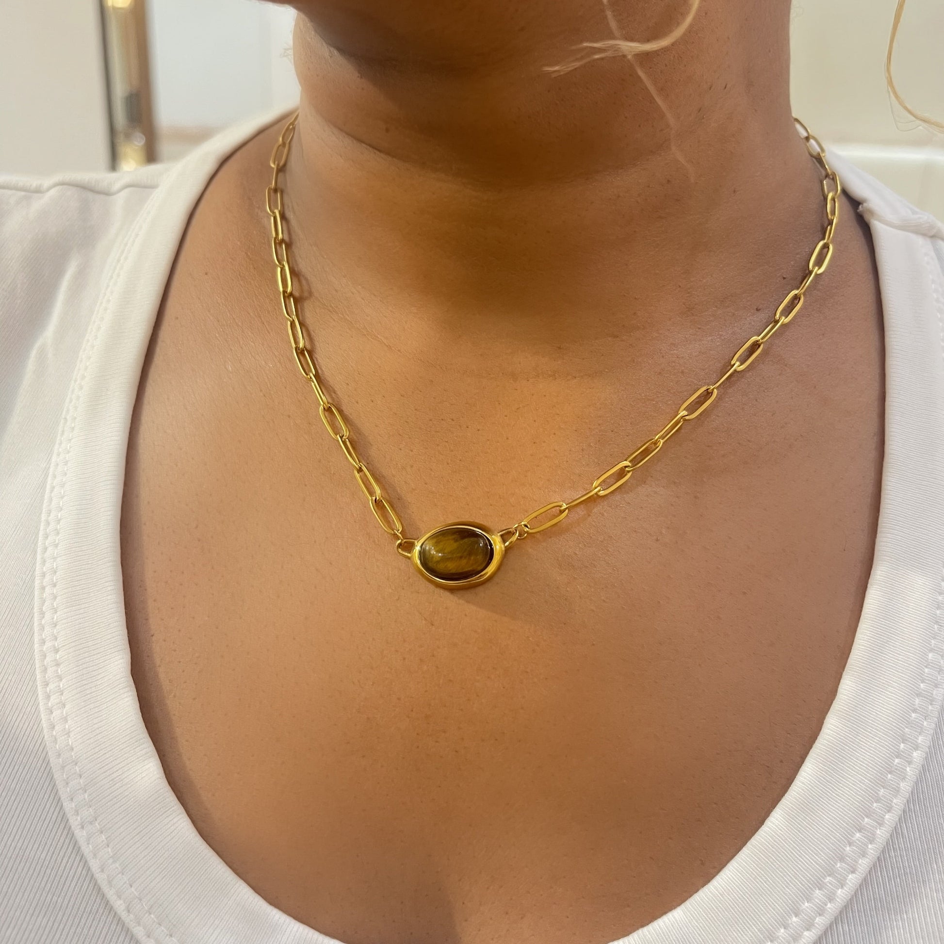 Gold chain necklace with a pendant on a person wearing a white top.