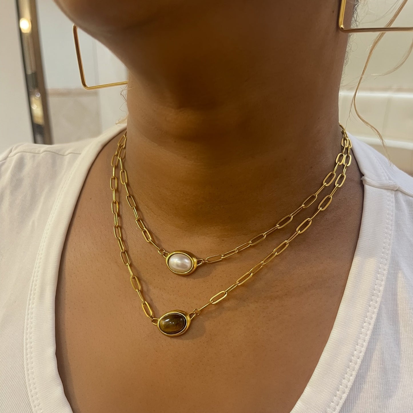 Gold chain necklaces with a pearl pendant on a white shirt.