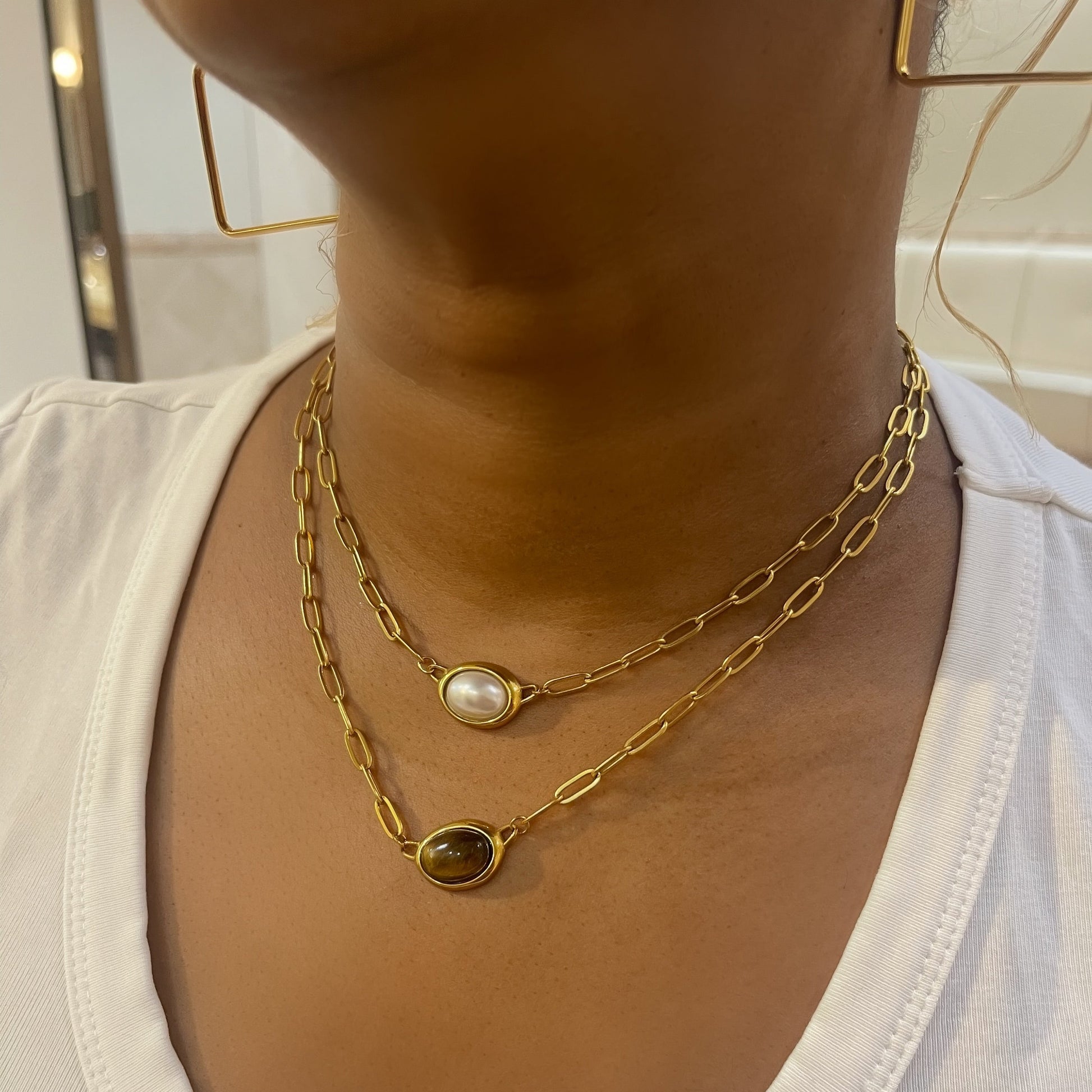 Gold chain necklaces with a pearl pendant on a white shirt.
