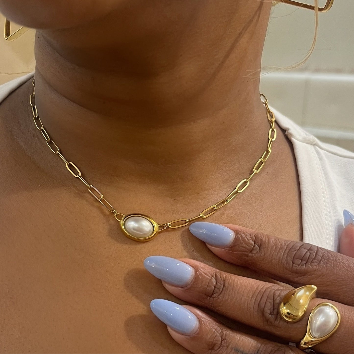 Person wearing a gold necklace and earrings with a hand resting on their chest.
