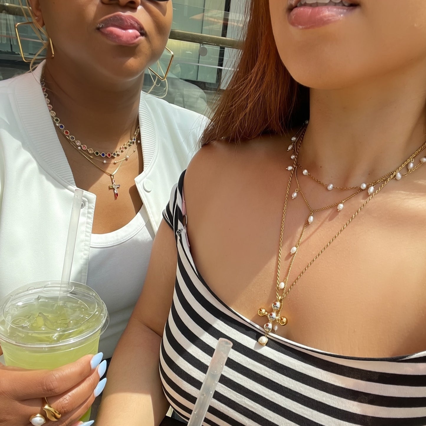 Two women sitting together, one holding a drink, with a blurred background.
