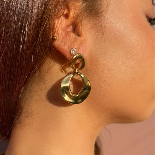 Close-up of a person wearing gold hoop earrings with a neutral background