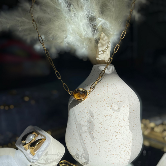 Gold necklace with a pendant on a textured white vase against a dark background