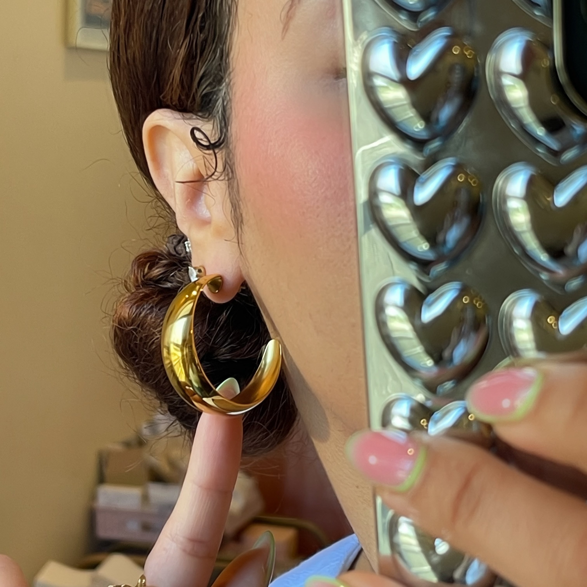 Person wearing a gold hoop earring with a decorative mirror in the background