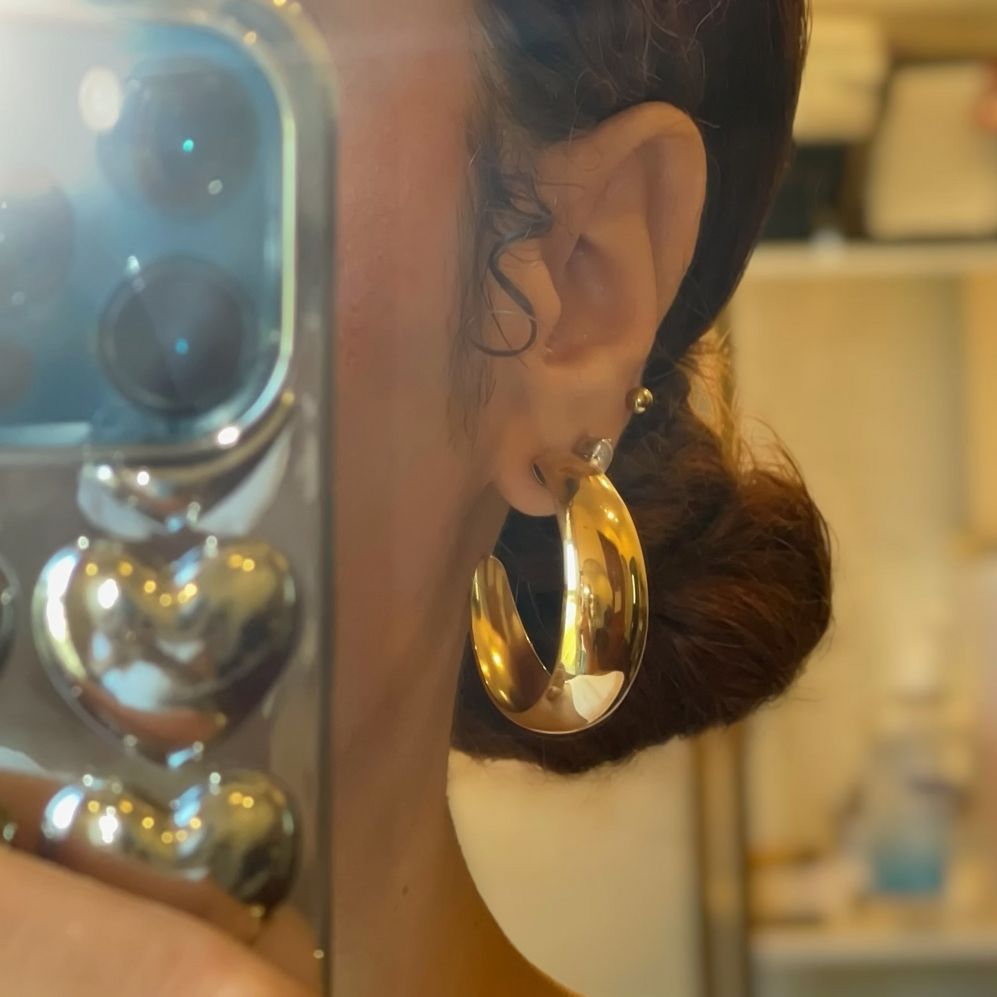 Person holding a phone wearing gold hoop earrings with a blurred background