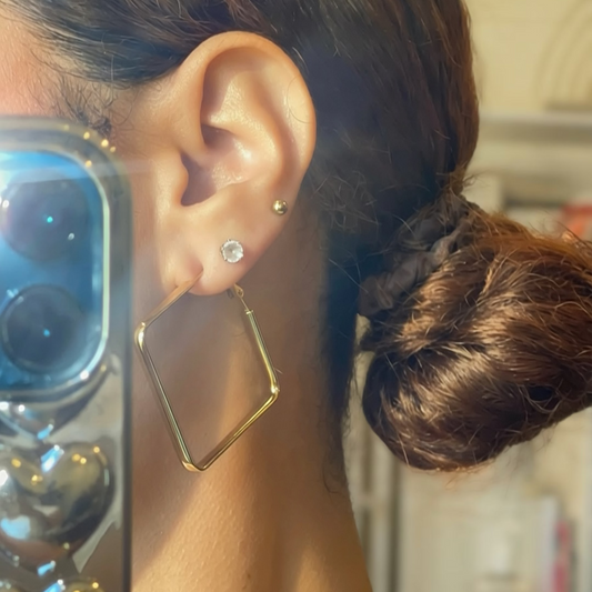 Close-up of a person wearing a gold hoop earring and holding a phone.
