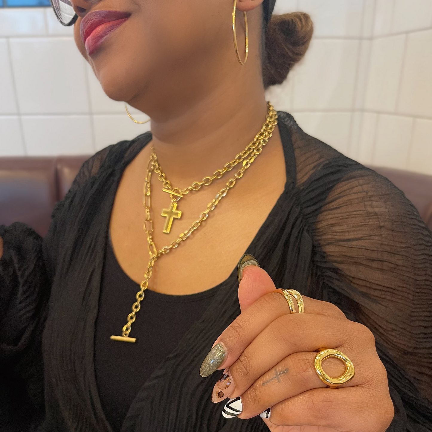 Person wearing gold jewelry including necklaces and rings, sitting indoors.