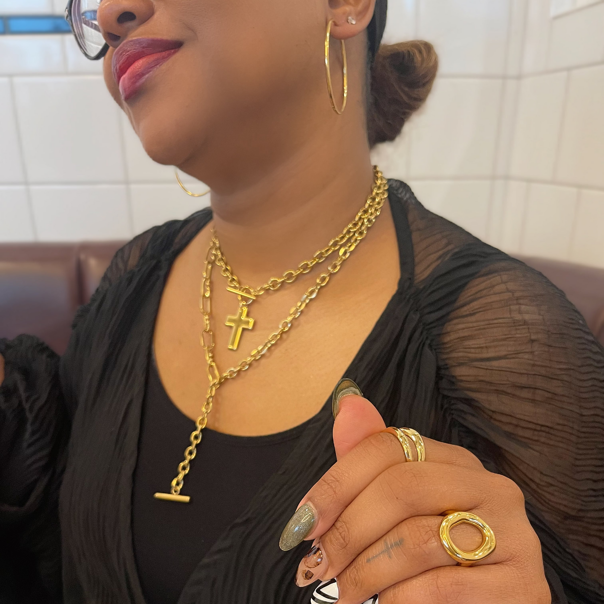 Person wearing gold jewelry including necklaces and rings, sitting indoors.