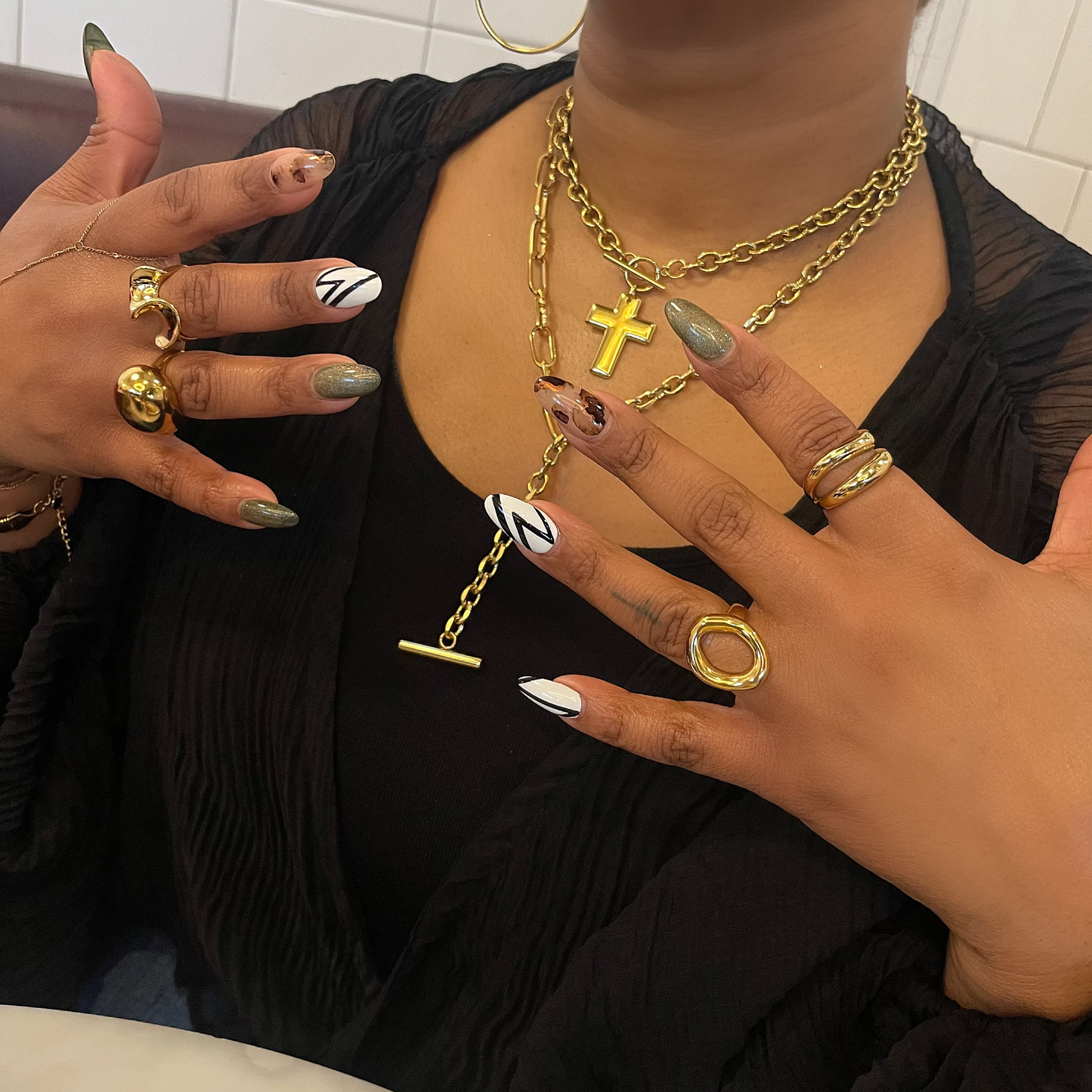 Person wearing gold jewelry with a black top and white tiled wall background