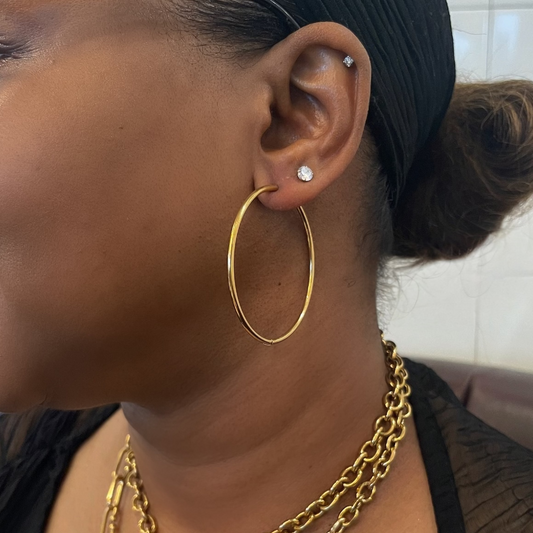 Woman wearing gold hoop earrings and necklaces with a blurred background