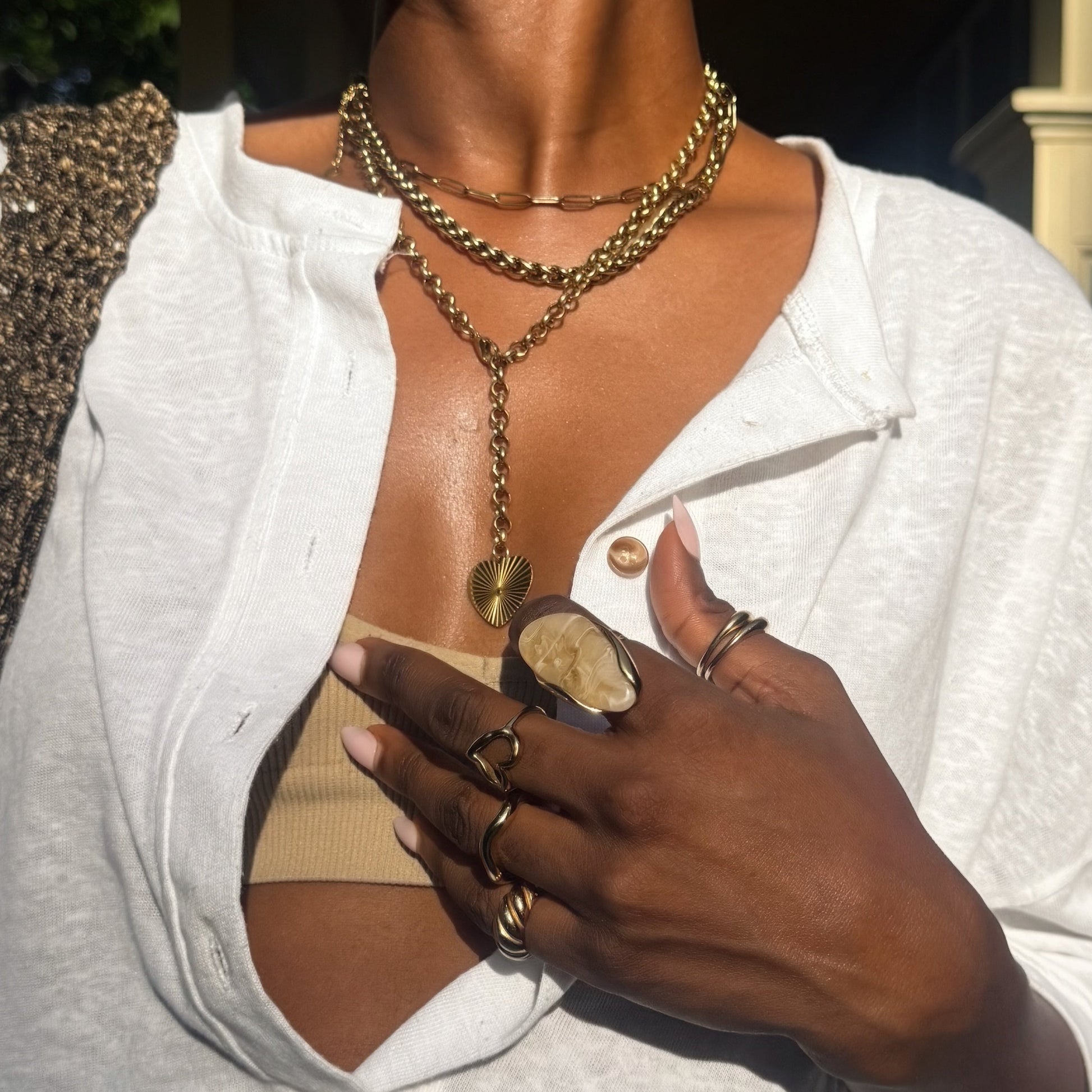Woman wearing sunglasses, a white shirt, and gold jewelry outdoors.