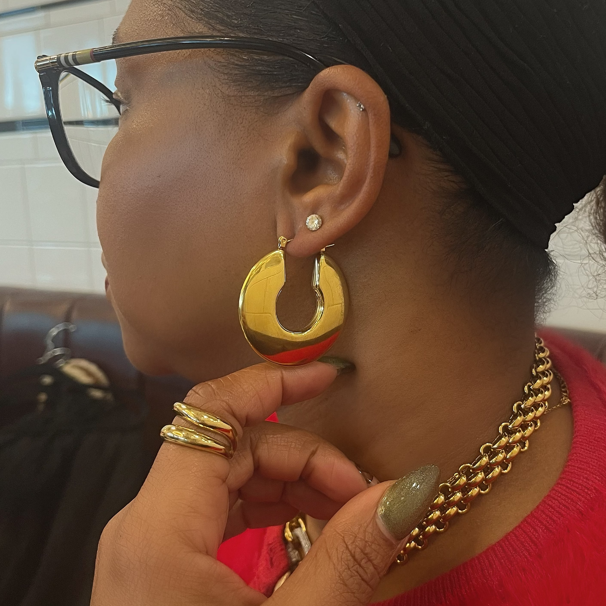 Woman wearing gold hoop earrings and a gold chain necklace, with a blurred background.