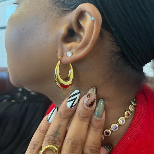 Close-up of an ear with gold hoop earrings and a hand with gold rings and colorful nail polish.