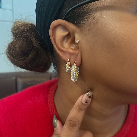 Close-up of a person wearing gold hoop earrings with a red garment and blue headscarf.