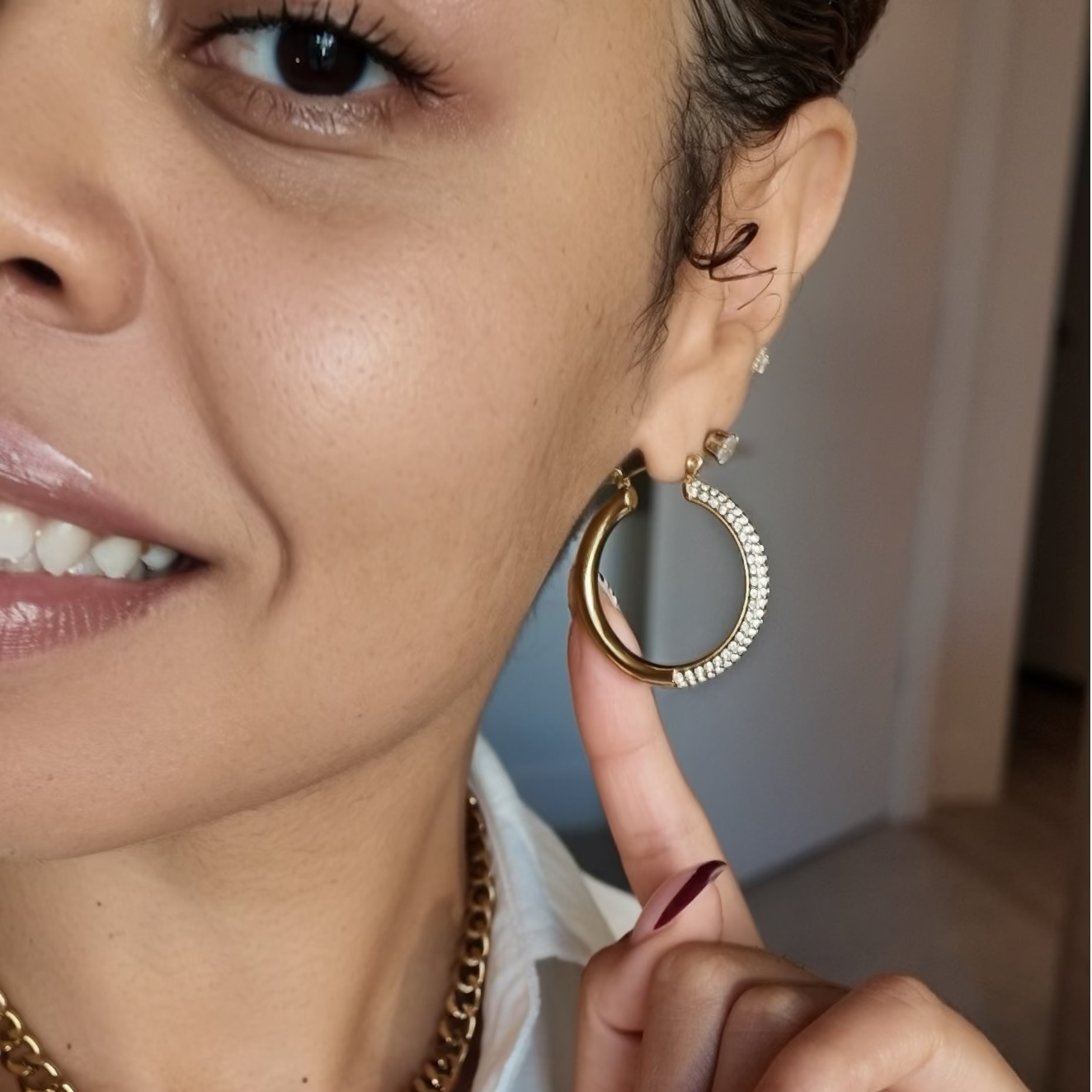 A close-up lifestyle shot of a woman wearing gold jewelry, featuring a gold chain necklace with a key pendant and matching gold hoop earrings.