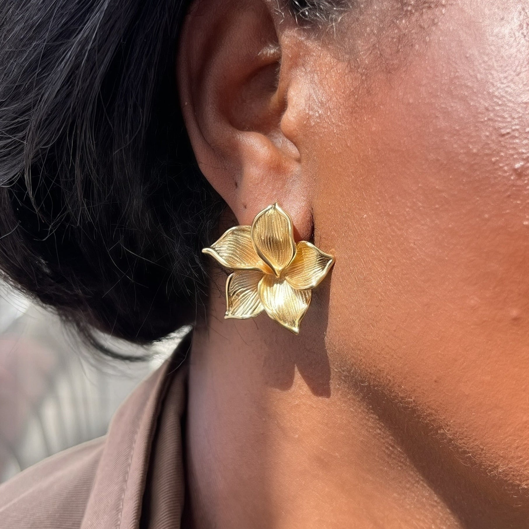 Gold flower-shaped earring worn by a person with a blurred background