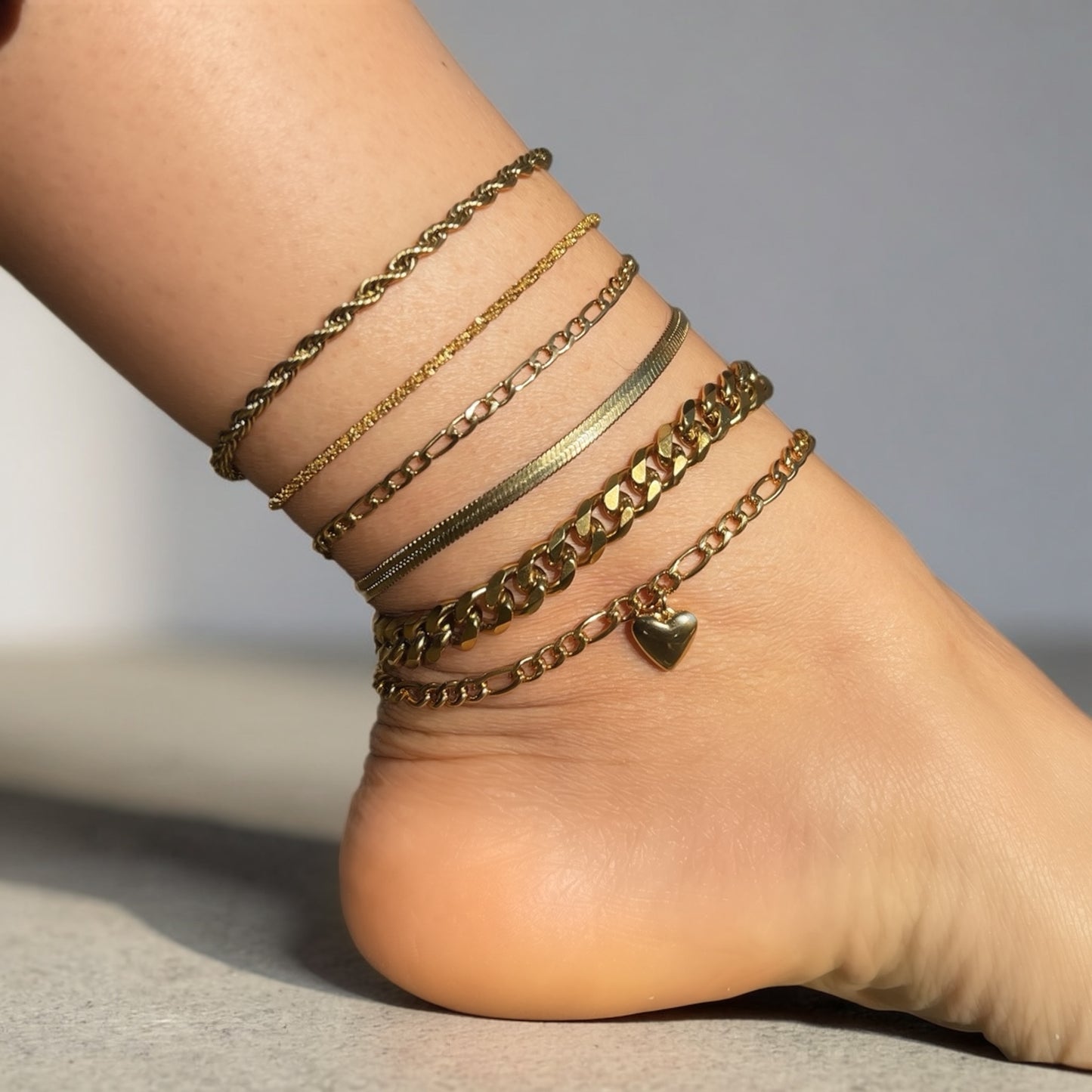 Multiple gold anklets on a foot against a neutral background