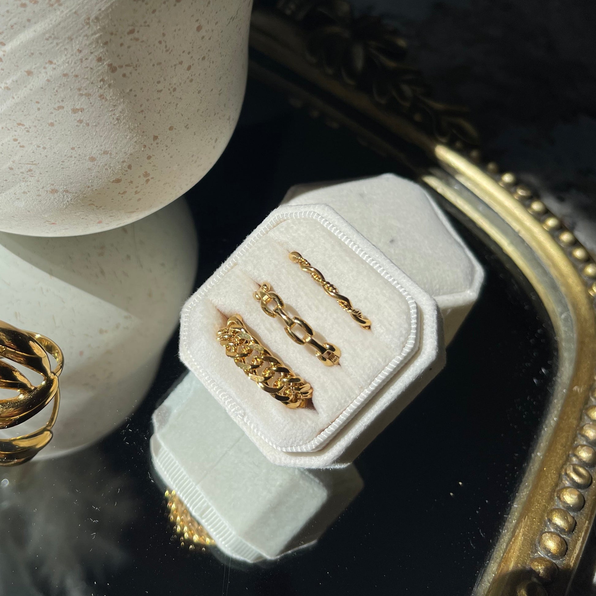 Gold rings on a white stone surface with a decorative mirror in the background