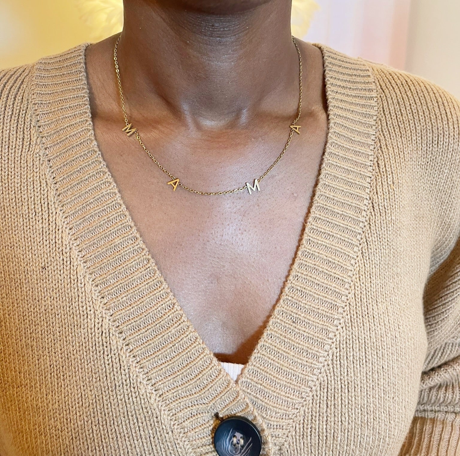 Gold necklace with MAMA on a person wearing a beige cardigan.