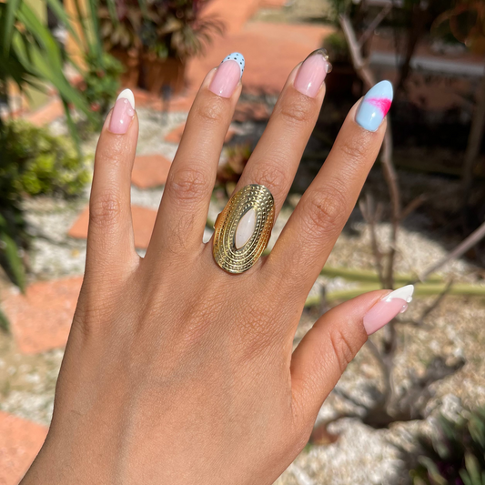 Hand wearing a gold ring with colorful nail polish against a garden background