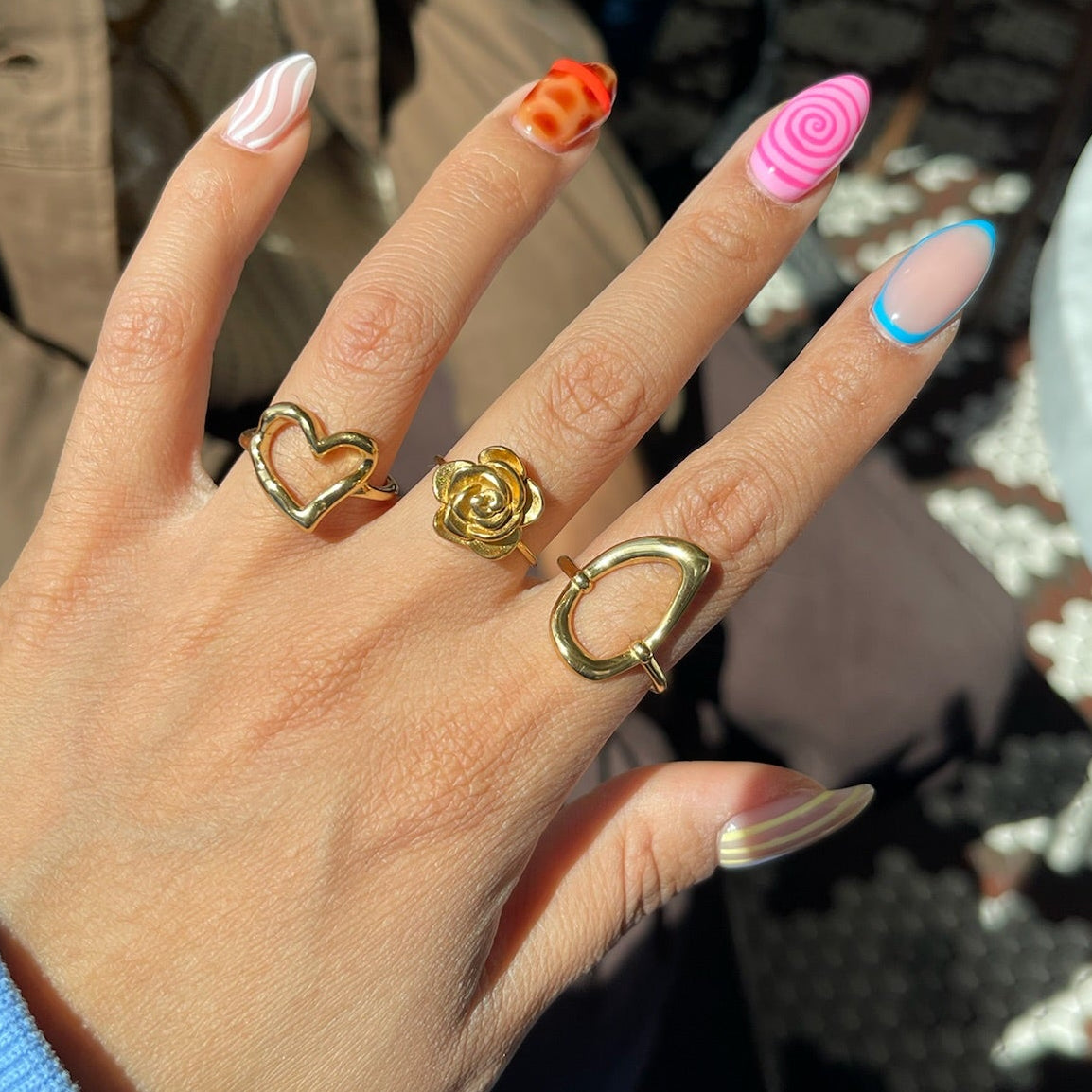 Hand with colorful nail polish and gold rings in an outdoor setting