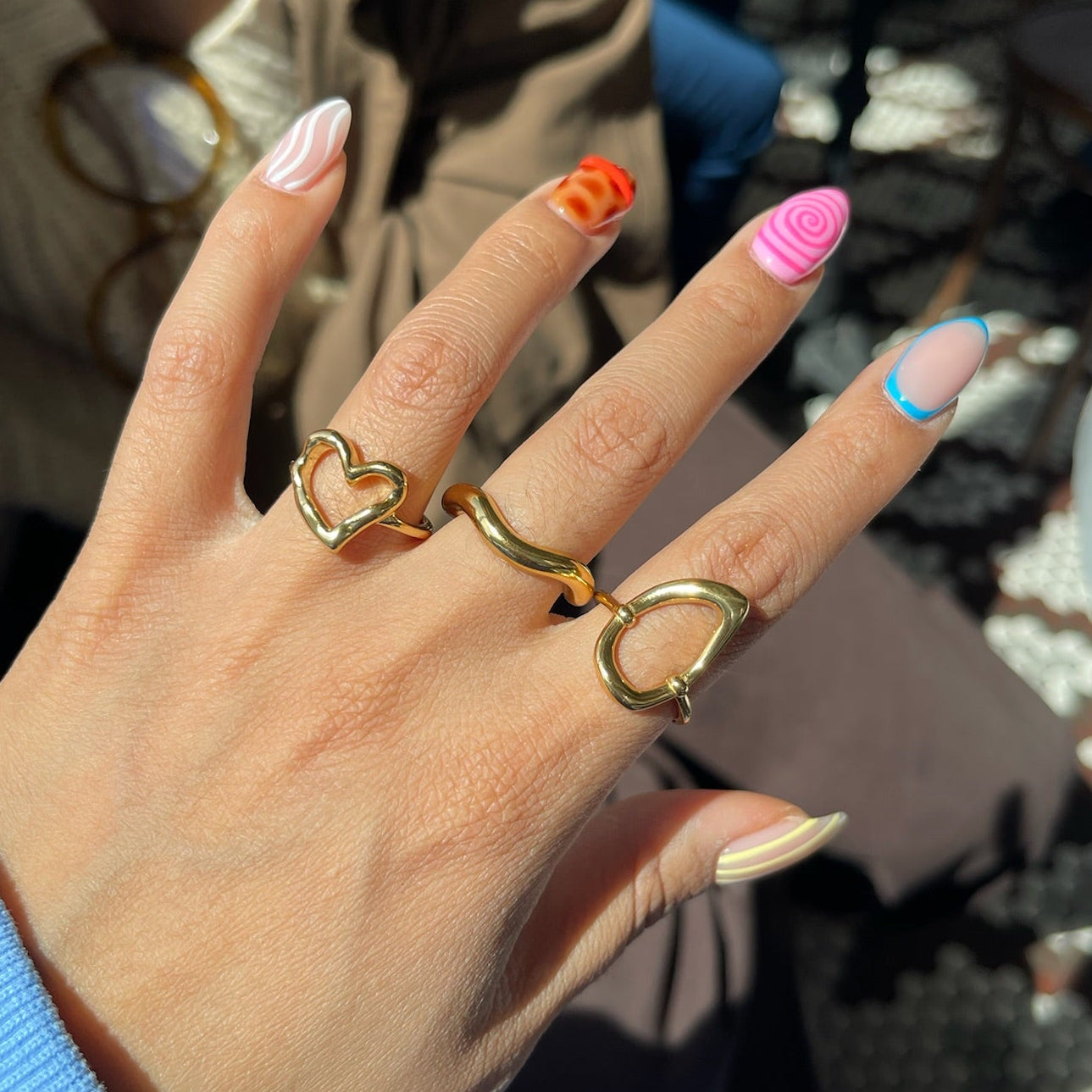 Hand with gold rings and colorful nails in an outdoor setting