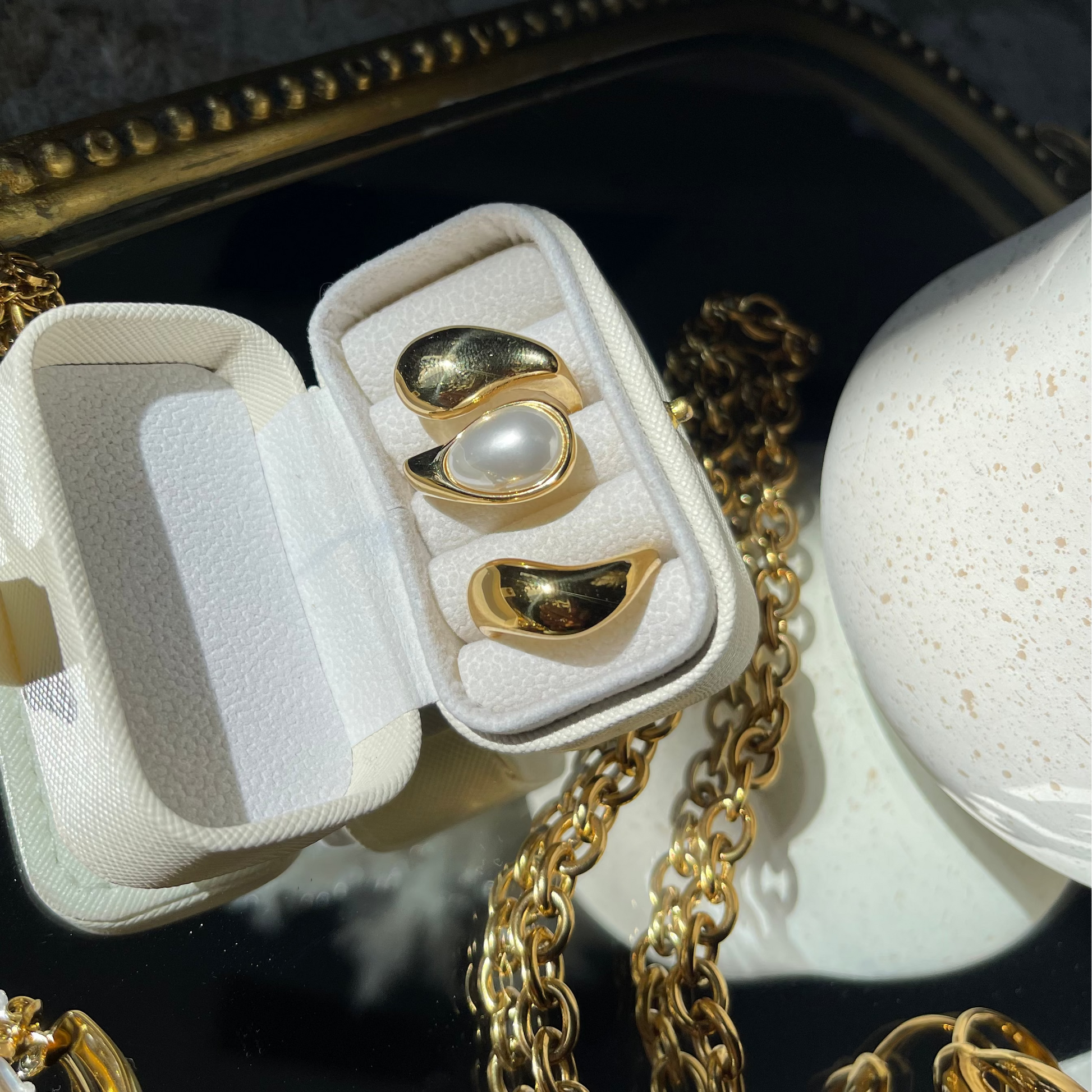 Gold earrings in a white case on a dark textured surface with a gold chain.