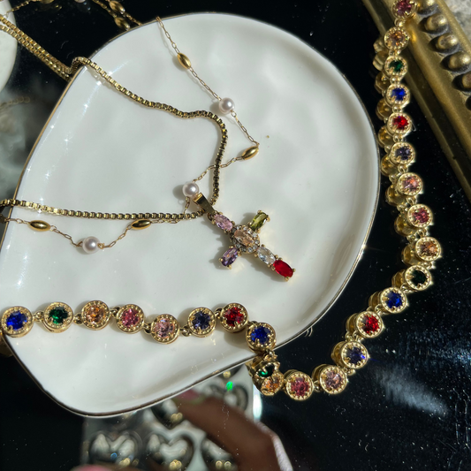 Jewelry set including a cross necklace and colorful necklace with gemstones on a white dish.