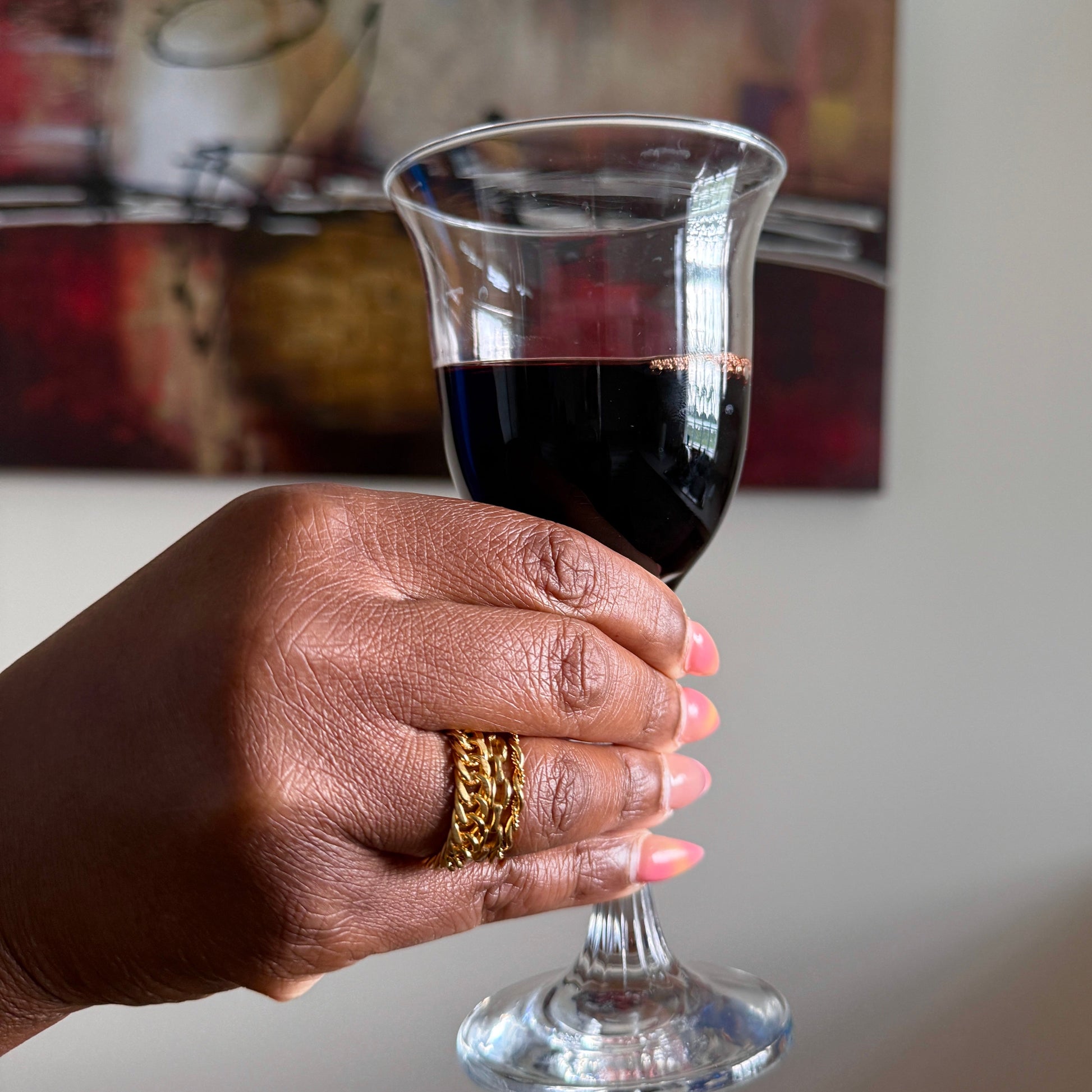 Hand with gold rings holding a glass of red wine with a blurred background