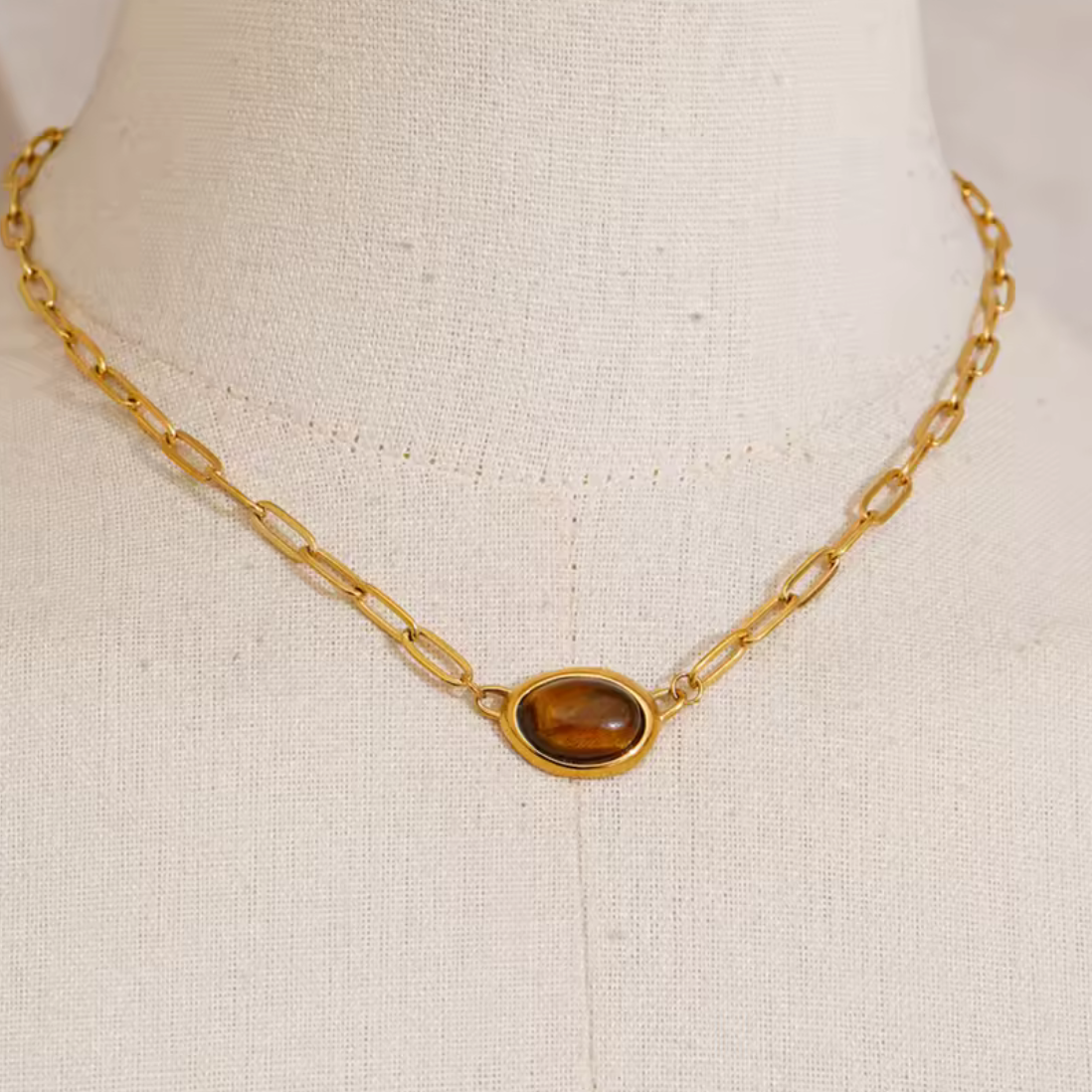 Gold necklace with a brown pendant on a mannequin bust.
