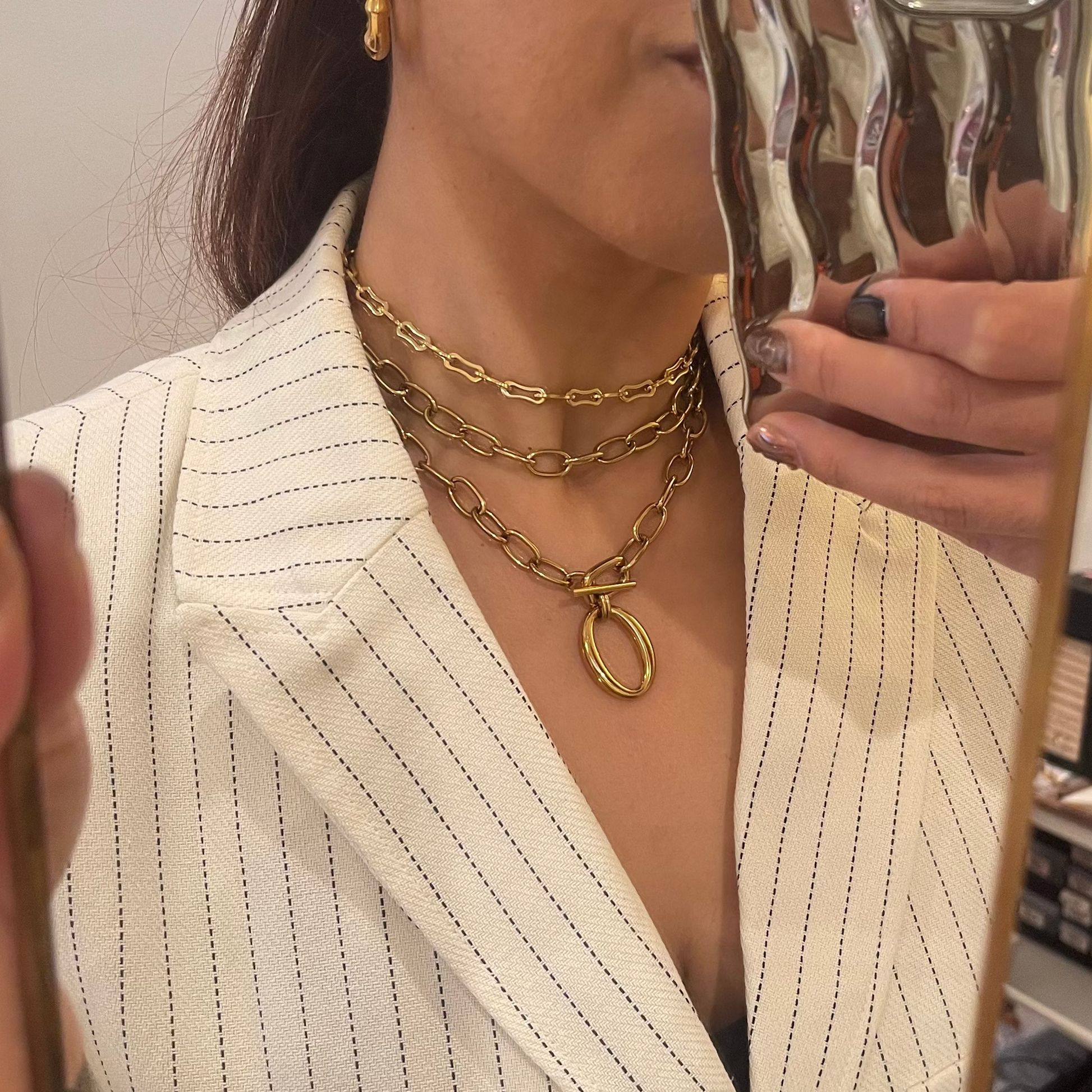 Person wearing a gold chain necklace in front of a mirror