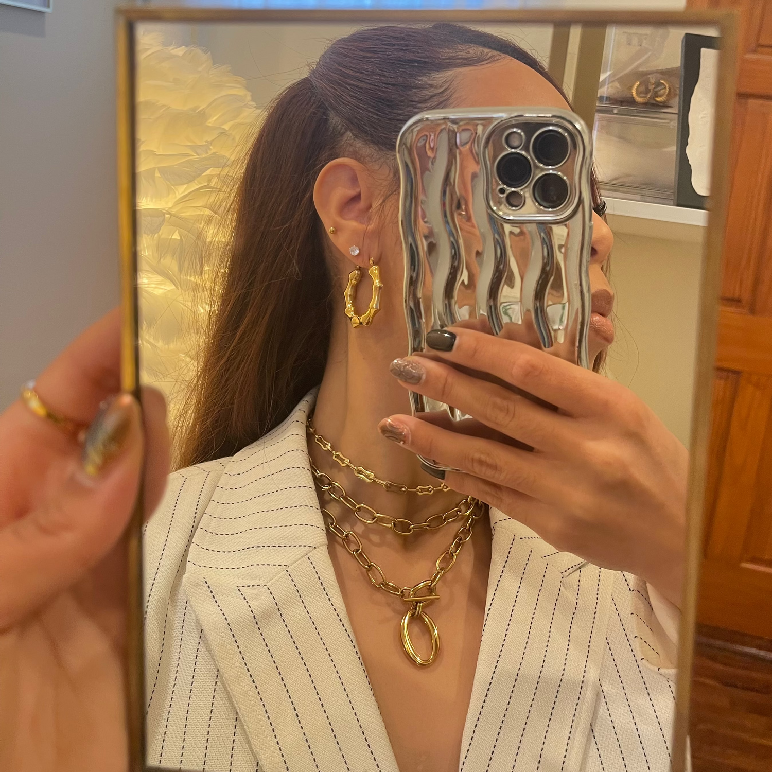 Person wearing gold jewelry taking a mirror selfie
