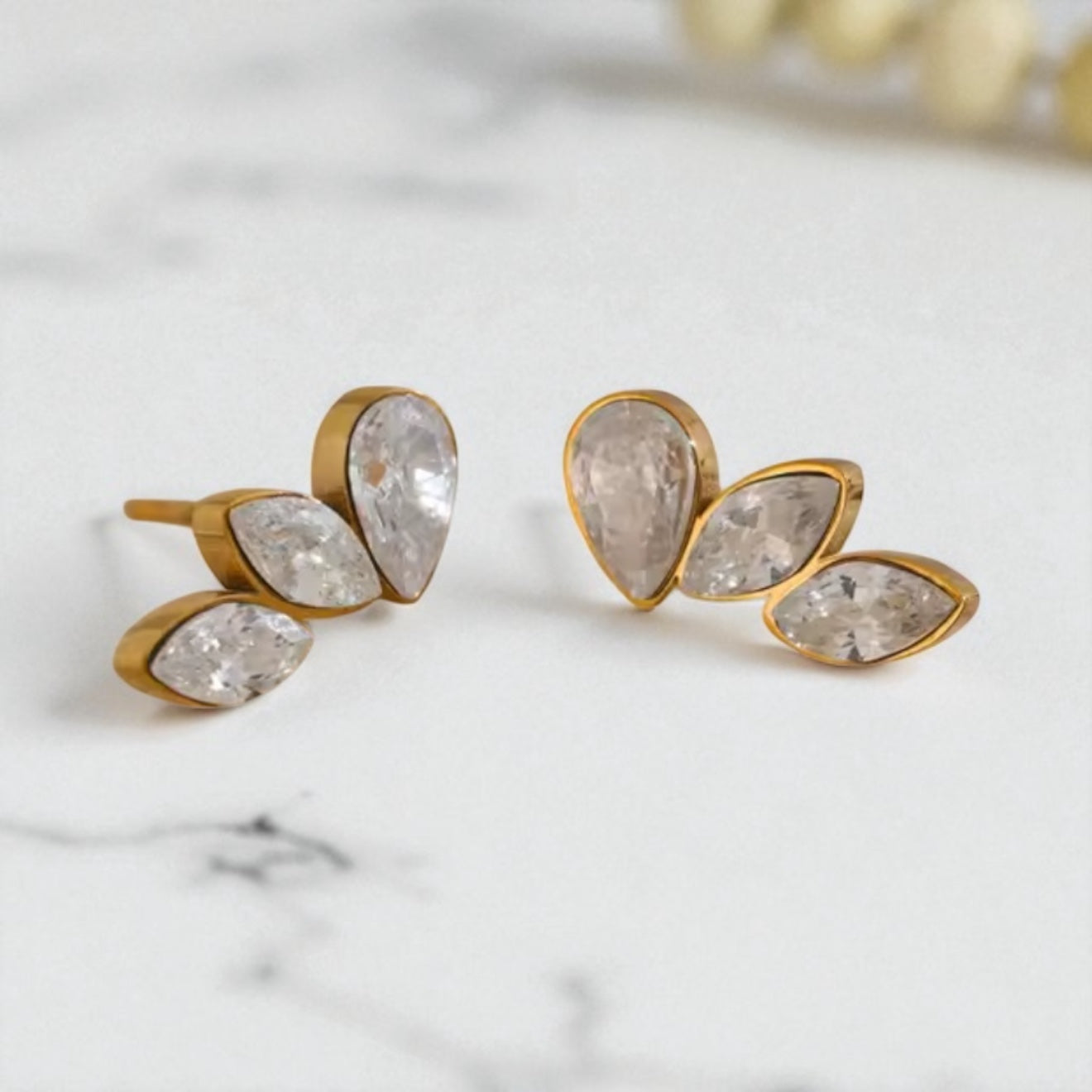 Gold stud earrings with clear gemstones on a marble surface