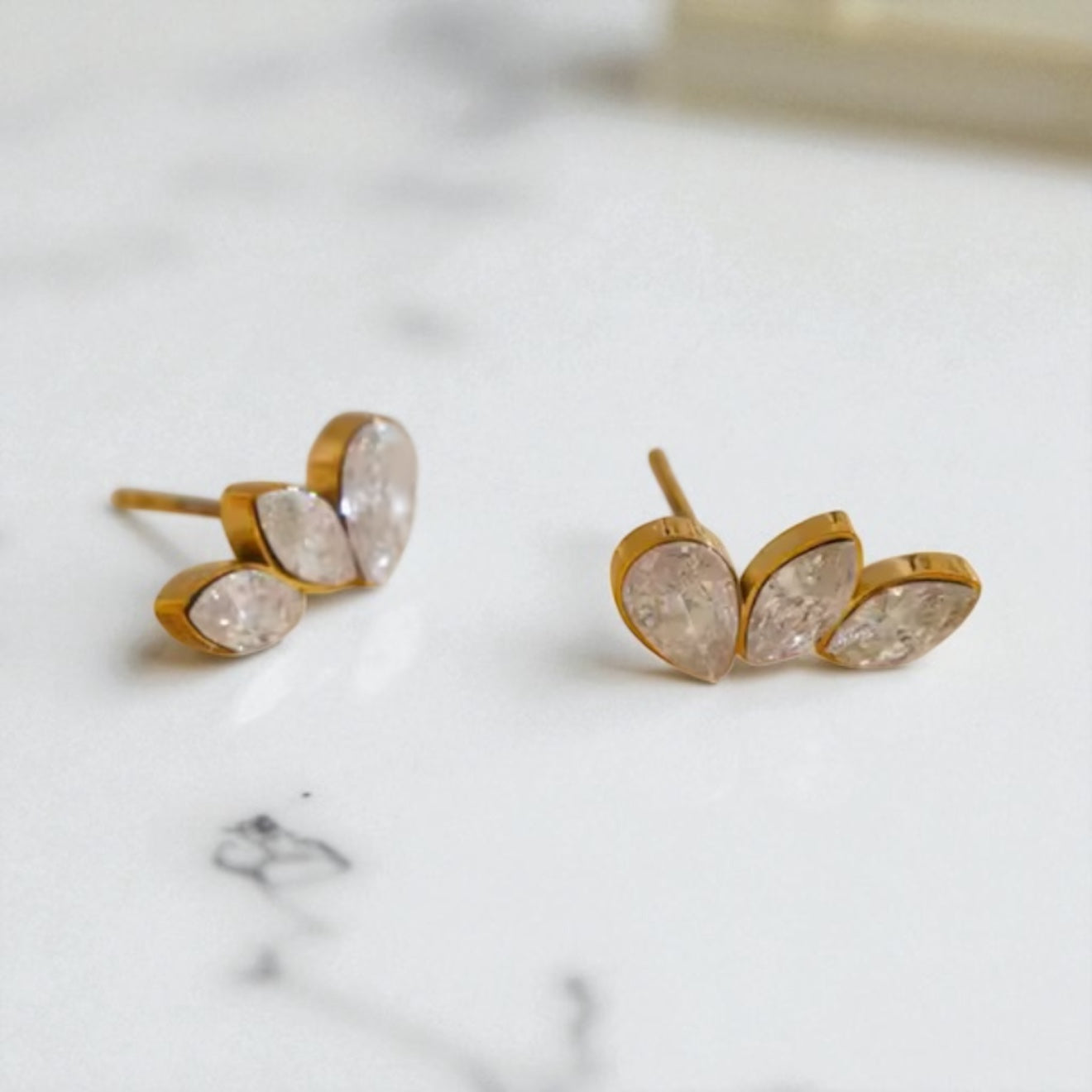 Gold leaf-shaped stud earrings with gemstone centers on a marble surface