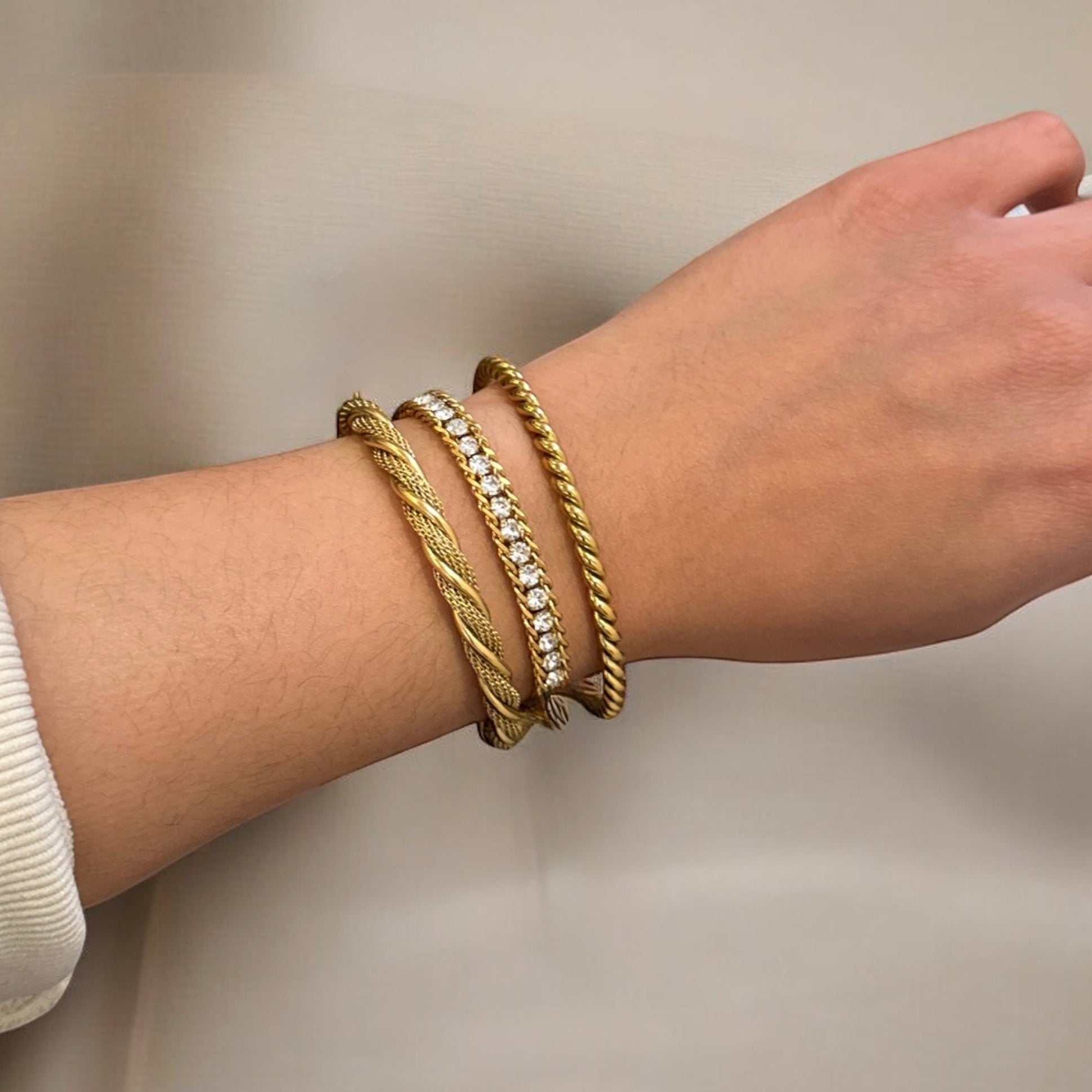 Close-up of a wrist wearing gold bracelets on a neutral background