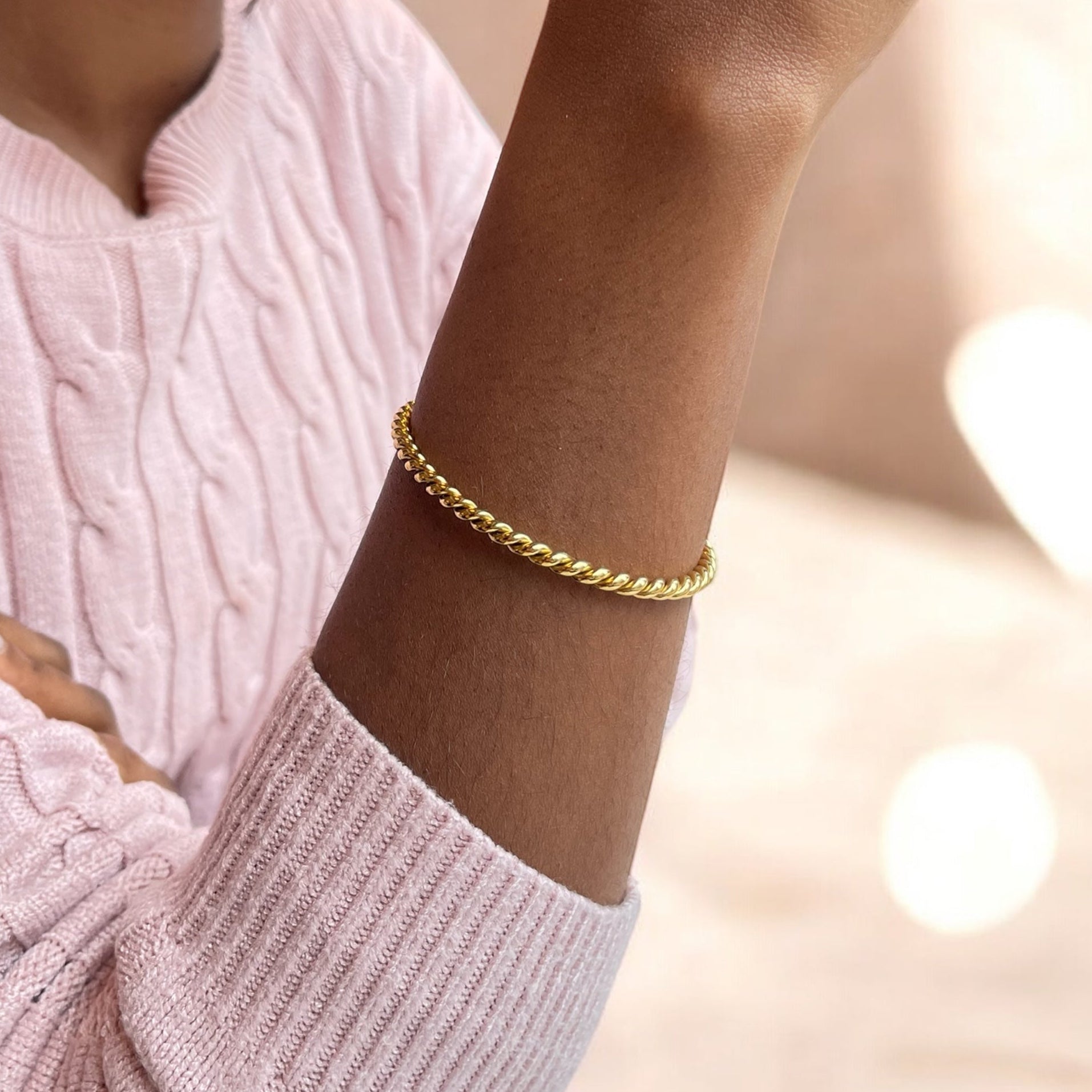 Gold bracelet on a person wearing a pink sweater with a blurred background