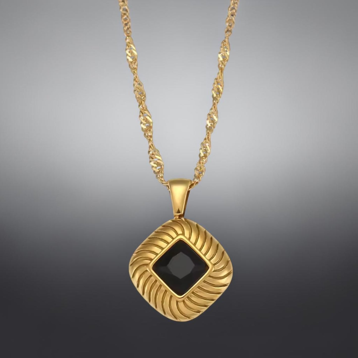 Gold necklace with a black square pendant on a gray background