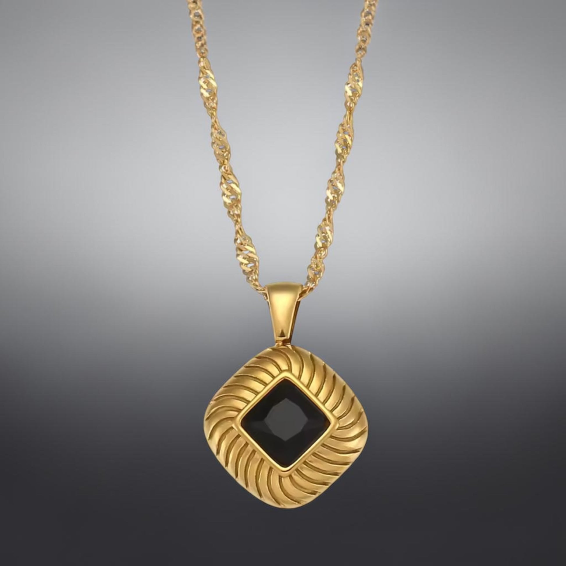 Gold necklace with a black square pendant on a gray background