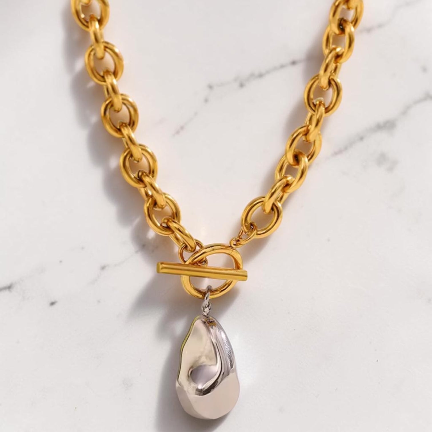 Gold chain necklace with a silver teardrop pendant on a marble background