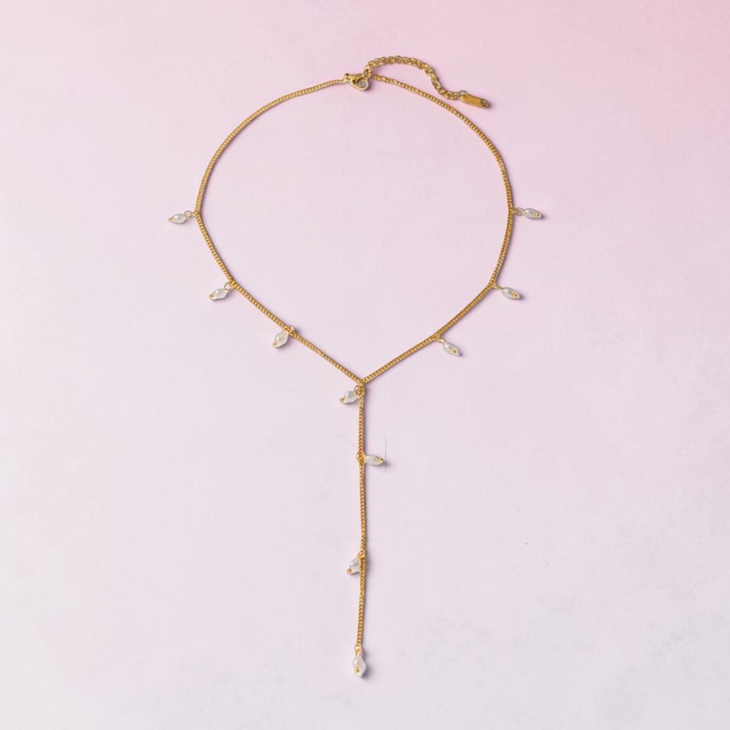 Gold necklace with small pearls on a light pink background