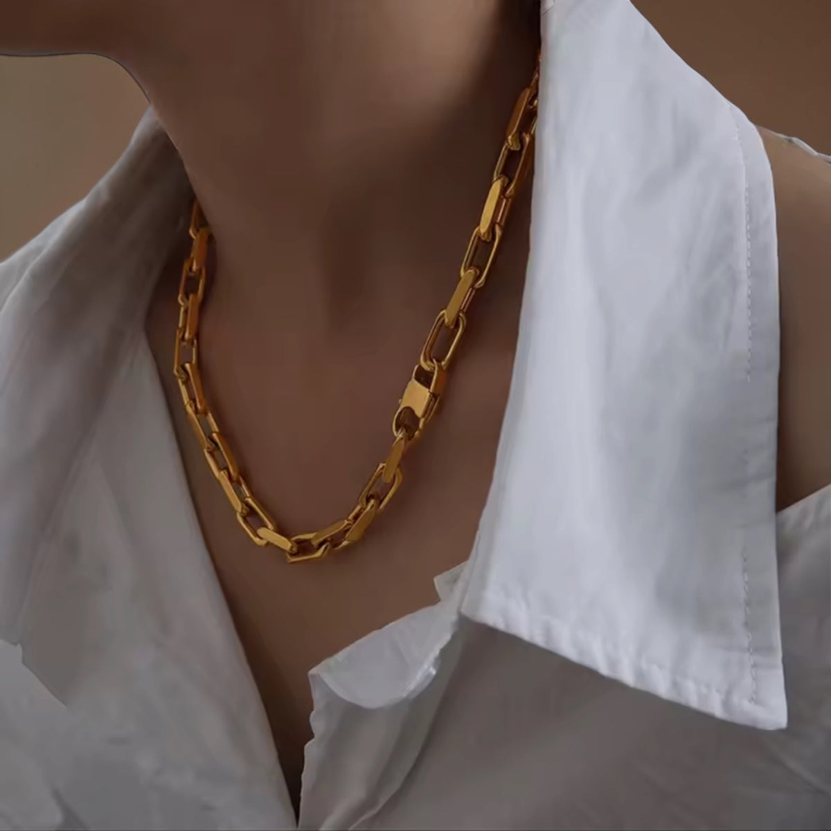 A close-up of a person wearing a chunky gold chain necklace with a white collared shirt.